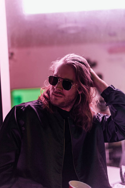 handsome young man in leather jacket and sunglasses spending time on street at night under pink light - Φωτογραφία, εικόνα