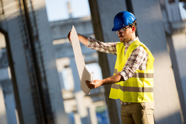 Portrait of male site contractor engineer with hard hat holding blue print paper at construction site, - Valokuva, kuva