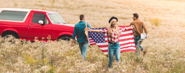 group of young friends with united states flag in flower field during road trip - Φωτογραφία, εικόνα