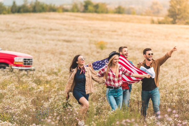 group of young american travellers with flag walking by flower field and pointing somewhere - Photo, Image