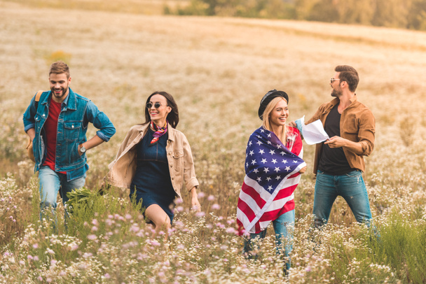 grupo de jóvenes americanos con bandera caminando por el campo de flores
 - Foto, Imagen