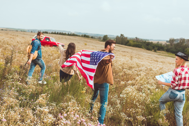 група щасливих молодих американських мандрівників з прапором, що йде по квітковому полю
 - Фото, зображення
