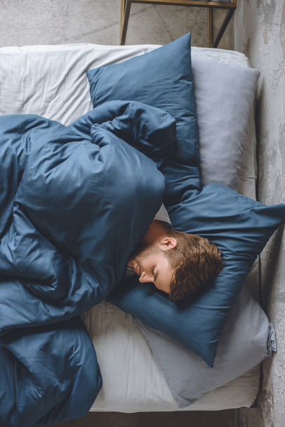 vista superior del joven hombre guapo durmiendo debajo de la manta en su cama en casa
 - Foto, imagen