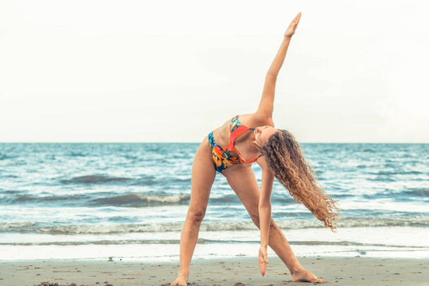 Young woman practicing yoga pose on the beach in summer. Healthy lifestyle and meditation. - Foto, imagen