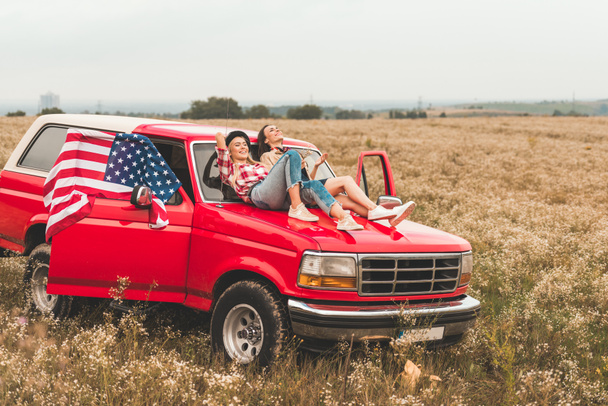 schöne junge Freundinnen entspannen sich auf der Motorhaube im Feld - Foto, Bild