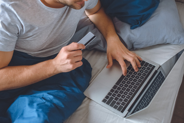 cropped image of man in bed with credit card doing online shopping on laptop  - Фото, изображение