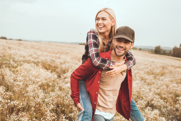 happy young woman piggybacking on boyfriend in flower field - Φωτογραφία, εικόνα