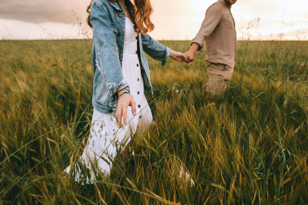 cropped view of couple holding hands and walking on green summer meadow - Foto, imagen