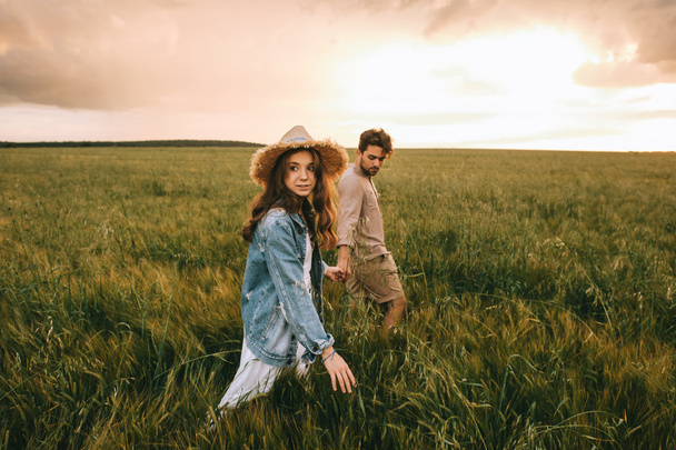 attractive stylish couple holding hands and walking on green meadow - Фото, изображение