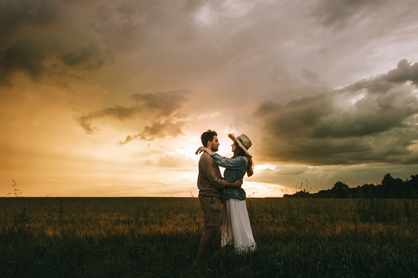 young stylish couple hugging on meadow at beautiful sunset - Fotó, kép