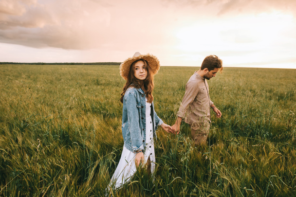 young stylish couple holding hands and walking on green meadow, love story - Fotografie, Obrázek