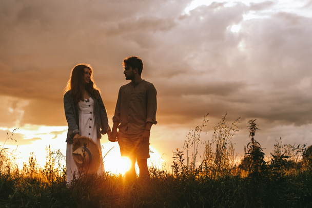 silhouette de couple tenant la main sur la prairie au coucher du soleil
 - Photo, image