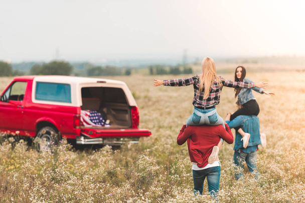 jeunes femmes chevauchant sur les épaules de copains sur le terrain pendant le voyage en voiture
 - Photo, image