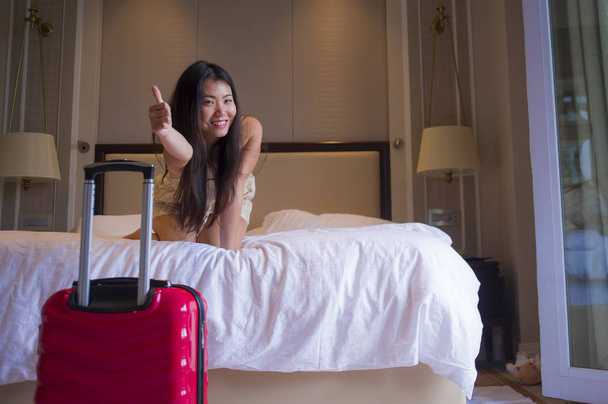 lifestyle portrait of young happy and beautiful Asian Korean tourist woman with travel suitcase just arrived at five star hotel room playing on bed enjoying excited in Summer holidays trip - Fotografie, Obrázek