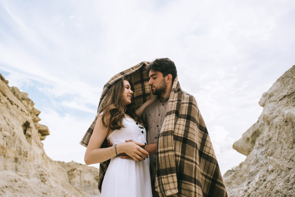 casal feliz abraçando sob cobertor em desfiladeiro de areia com céu nublado
 - Foto, Imagem