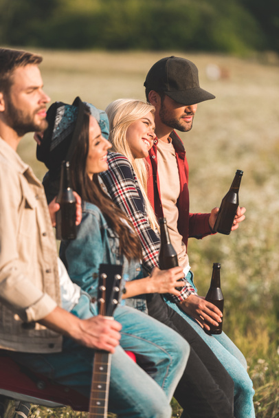 группа молодых людей, пьющих пиво, сидя в багажнике автомобиля в поле
 - Фото, изображение