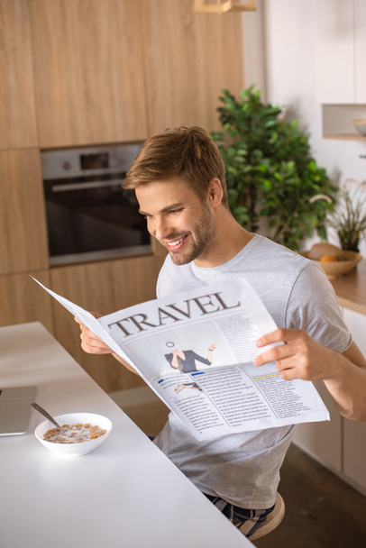 smiling man reading travel newspaper at kitchen table with breakfast - Foto, Imagen