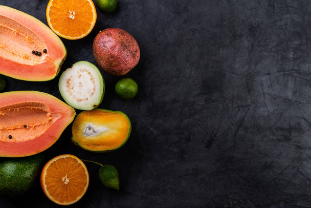 Tropické ovoce, papája, guava, vášeň, vápno a oranžové na tmavém pozadí, pohled shora - Fotografie, Obrázek