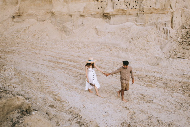 μεγάλη γωνία προβολής ζευγάρι κρατώντας τα χέρια και το περπάτημα στην άμμο φαράγγι - Φωτογραφία, εικόνα