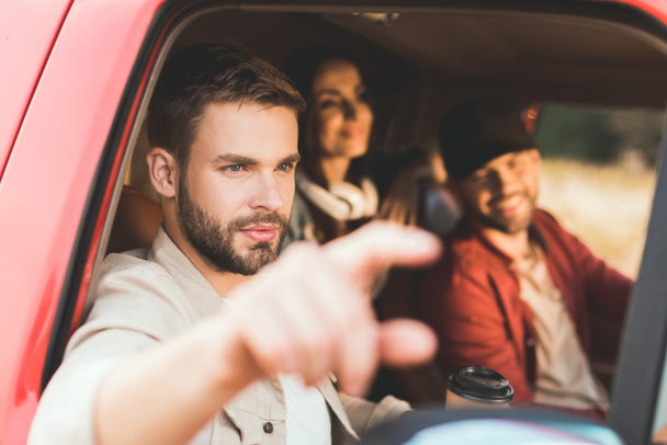 joven guapo señalando en algún lugar mientras monta coche con amigos
 - Foto, Imagen