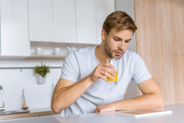 man drinking fresh juice during breakfast at kitchen table with digital tablet  - 写真・画像