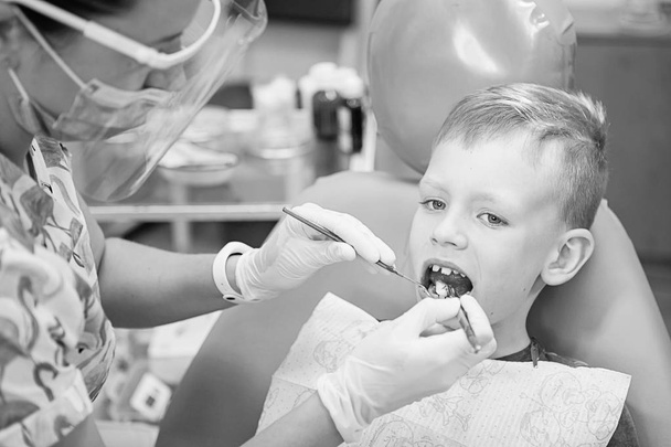 Egy kisfiú a fogorvos fogászati klinika recepcióján. Gyermek fogászat, gyermek fogászat. Fekete-fehér, retro stílusú fotózás. Orális egészség és higiénia - Fotó, kép