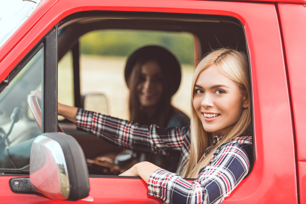 side view of smiling young girlfriends riding car and looking at camera - Foto, immagini