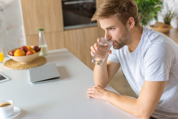 selective focus of young man drinking water at kitchen table  - Photo, Image