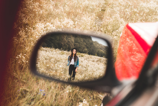 auto side mirror reflection of beautiful young woman walking in flower field alone - Photo, Image