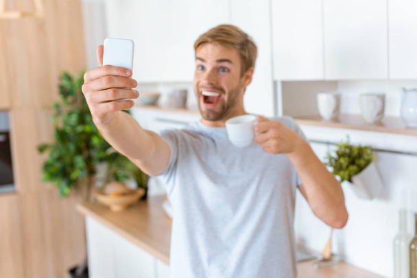 happy young man with coffee cup taking selfie on smartphone at kitchen - Фото, зображення