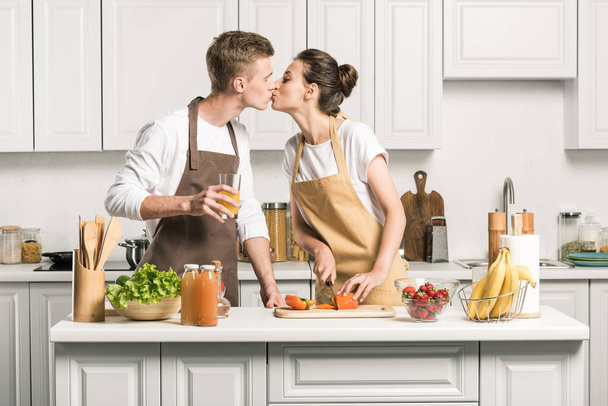 young couple kissing while cooking salad in kitchen - Zdjęcie, obraz