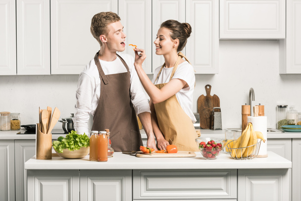girlfriend feeding boyfriend with piece of bell pepper in kitchen - Foto, Imagem