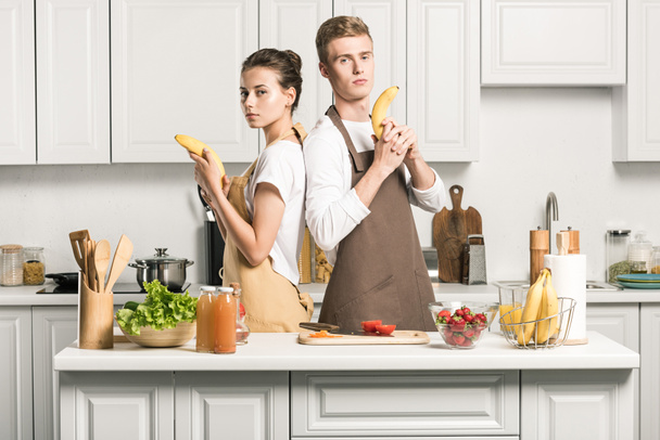 pareja joven divirtiéndose y sosteniendo armas de plátano en la cocina
 - Foto, Imagen