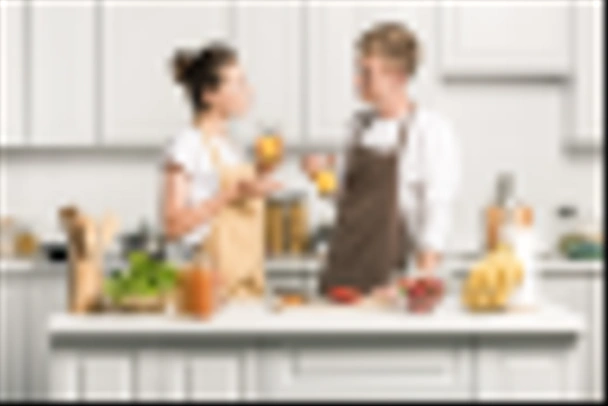 young couple cooking salad and holding glasses of healthy juice in kitchen - Photo, Image