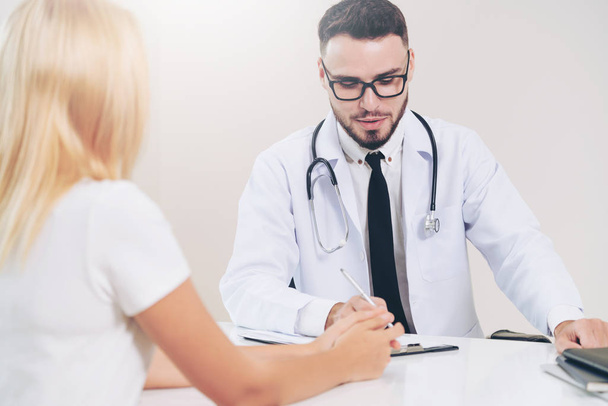 Male doctor is talking to female patient in hospital office. Healthcare and medical service. - Photo, Image