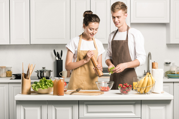 pareja joven cocinar ensalada y añadir especias en la cocina
 - Foto, imagen