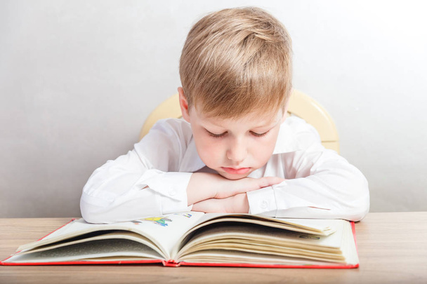 child in a white shirt sitting with a book at his Desk on white background - Foto, imagen