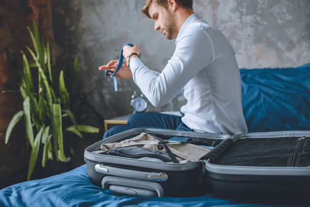 selective focus of businessman packing luggage in suitcase in bedroom at home - Φωτογραφία, εικόνα