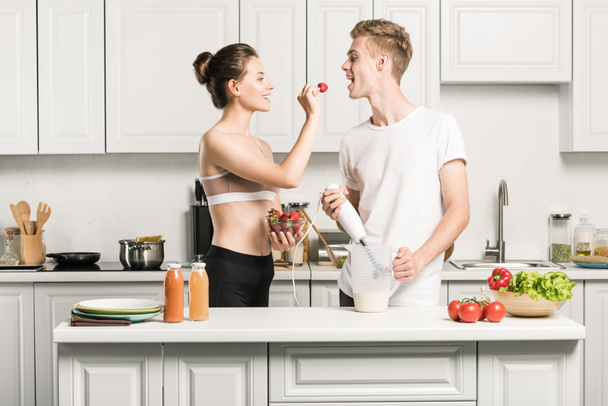 girlfriend feeding boyfriend with strawberry in kitchen - Photo, Image