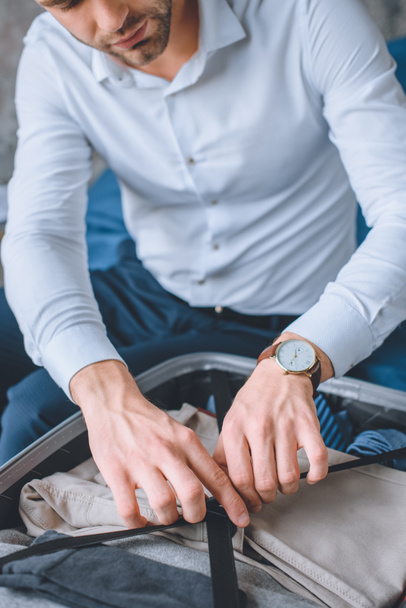 selective focus of businessman with wristwatch packing luggage in suitcase  - Φωτογραφία, εικόνα