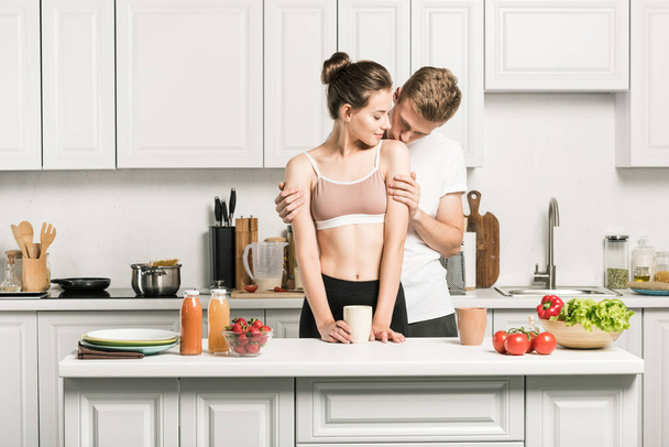 boyfriend kissing girlfriends shoulder in kitchen - Fotografie, Obrázek
