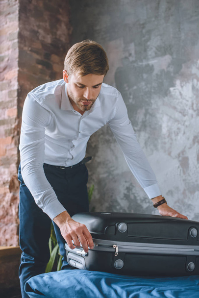 young businessman closing suitcase in bedroom at home   - Fotoğraf, Görsel