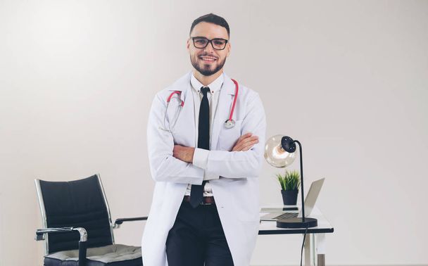 Male doctor crossed arms standing at office table in the hospital. Medical and healthcare concept. - Zdjęcie, obraz