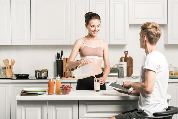 fidanzata versando latte e fidanzato utilizzando tablet in cucina
 - Foto, immagini