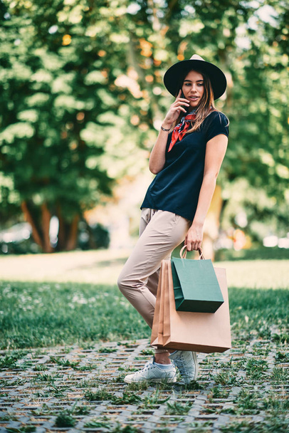Retrato de mulher usando telefone inteligente e de pé no parque depois de fazer compras
. - Foto, Imagem