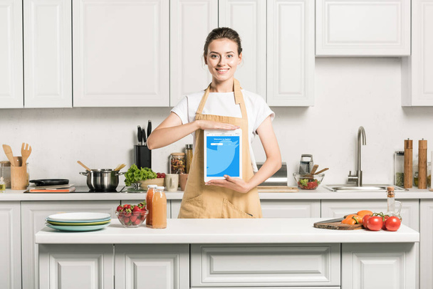 привлекательная девушка держит планшет с загруженной странице Twitter на кухне
 - Фото, изображение