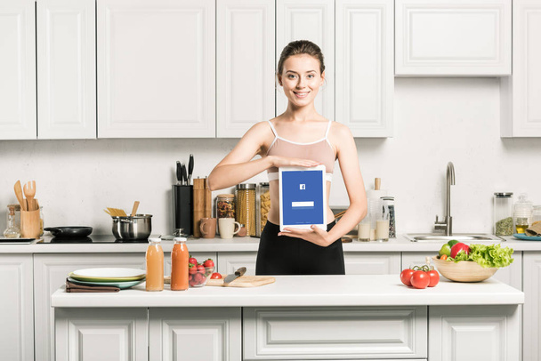 attrayant fille tenant tablette avec page facebook chargé dans la cuisine
 - Photo, image