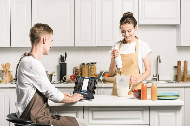 novia cocina y novio usando el ordenador portátil con página linkedin cargado en la cocina
 - Foto, imagen