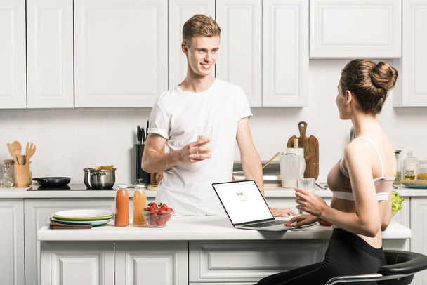 novia usando el ordenador portátil con página de google cargado y mirando novio en la cocina
 - Foto, imagen