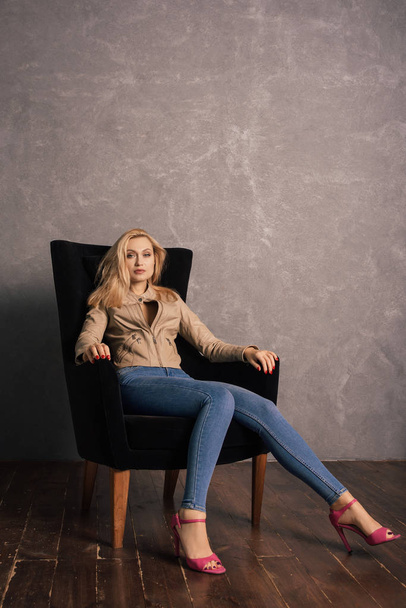 Adalt lady in jeans and a leather jacket sitting on the armchair having a rest - Foto, Imagem